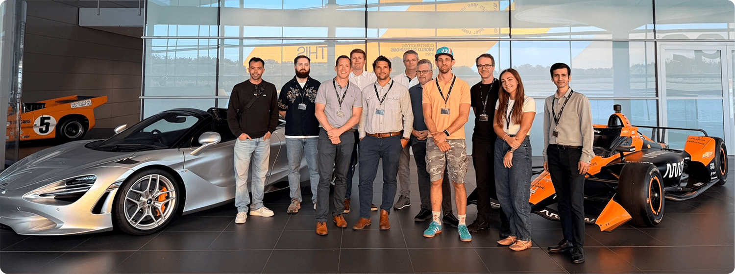 Group photo with McLaren supercar and Formula 1 car in a showroom.